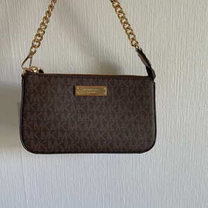 Michael Kors Clutch - Säljer min fina Michael Kors väska, den är knappt använd med taggen fortfarande på! En brun pouche väldigt inne just nu <3