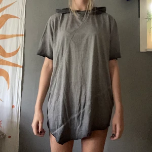 Grå washed T-shirt med luva - Grå washed tshirt med luva och asymmetriska sömmar och dragsko. Oversized. Kanske är menat att vara en klänning. Frakt tillkommer.