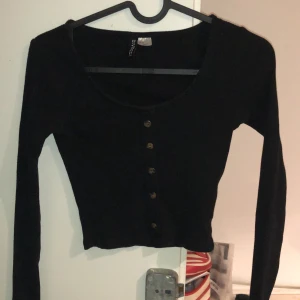 Svart topp med knappar  - Svart tight topp med bruna knappar. Superfin och stretchig. Är i storlek XS men passar även folk med S. Rund urringning och är långärmad.