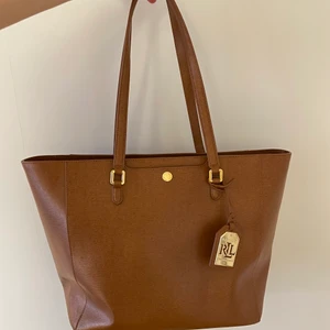Ralph lauren väska - En stor stilren Ralph lauren väska i färgen tan. Den har ett stort huvudfack med tre innerfack. Stängs med dragkedja. 100% läder. Nypris ca 2800kr. Väldigt fint skick!