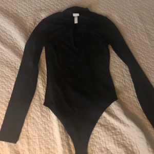 Svart bodysuit  - Svart body suit med en öppning vid bröst delen. Ny, inga fläck eller hål.