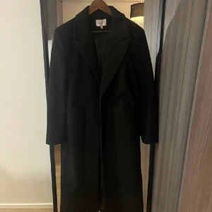Svart Kappa  - Svart lång kappa från Josefin HJ kollektionen på NAKD. Går ner till smalbenen på mig som är 1,68!