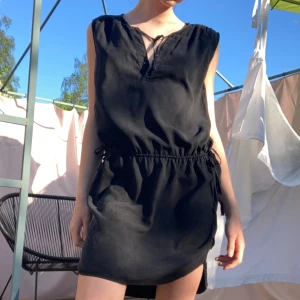 Klänning - Super snygg svart klänning som sitter lite puffigare ovanför midjan. Sedan knyter man snören på båda sidorna av höften till små rosetter🫶🏼