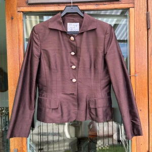 Mochino skjorta  - Mycket elegant kavaj i fint brunt med knappar av snäcka.  Material på 100% silke.  Kavajen har en klassisk design med en smal passform.   Storlek 38  Mycket bra skick, dock fattas 1 knapp längst ner på kavajen och inte provat ersätta den.