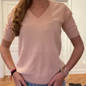 Ljusrosa kortärmad tröja - En ljusrosa kortärmad tröja med v-ringning. Tröjan har ribbstickade muddar vid ärmslut och nederkant. Tröjan är i hundra procent kashmir och från Lisa yang. 