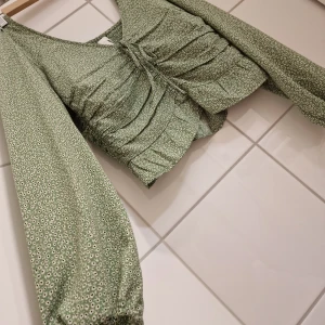 Croppad topp (Nyskick) Strl S - Croppad topp  Strl S Nyskick! Färg: Grön, Vit H&M  Superfin croppad topp i småblommigt mönster. Fina detaljer, dragsko fram, smock i ryggen. Endast använd en gång!