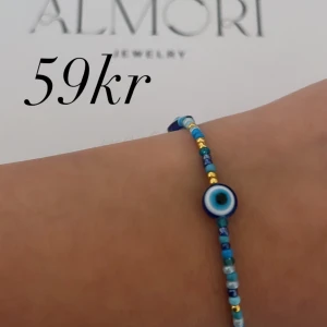 Flerfärgat armband med öga - Ett vackert armband med pärlor i olika färger och ett centralt öga. Armbandet har en mix av blå, guld och vita pärlor.