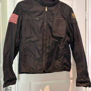 Ralph Lauren jacka M - Aldrig använd så snygg Ralph Lauren vaxad jacka. Bara att inse den inte kommer passa en kurvig kropp. Storlek M. Mörkblå med amerikanska flaggan på ena ärmen. 