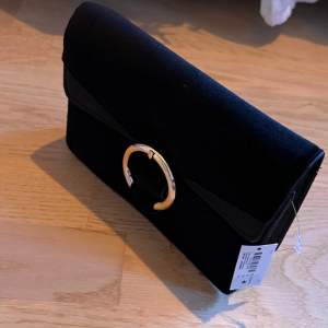 Svart kuvertväska i sammet material med en guldig detalj, aldrig använd 