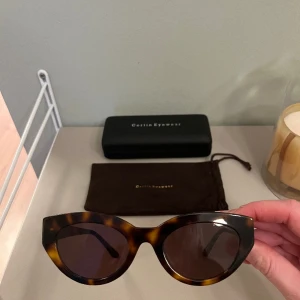 Gaby Solglasögon Corlin Eyewear Tortoise/Brown - Solglasögon i sköldpaddemönster/tortoise i Cat Eye modell. Säljs inklusive fodral, påse. Inköpta 2022 på Nelly. Använda 1-2 gånger enbart pga passar inte mitt ansikte så absolut nyskick. Nypris 1100kr