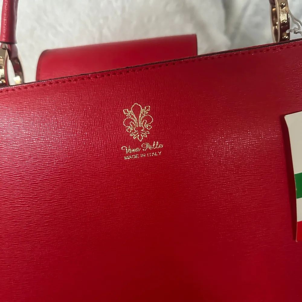 En fin röd väska i läder köpt i Italien oanvänd med band och prislapp, stor o rymlig med fack i!. Väskor.