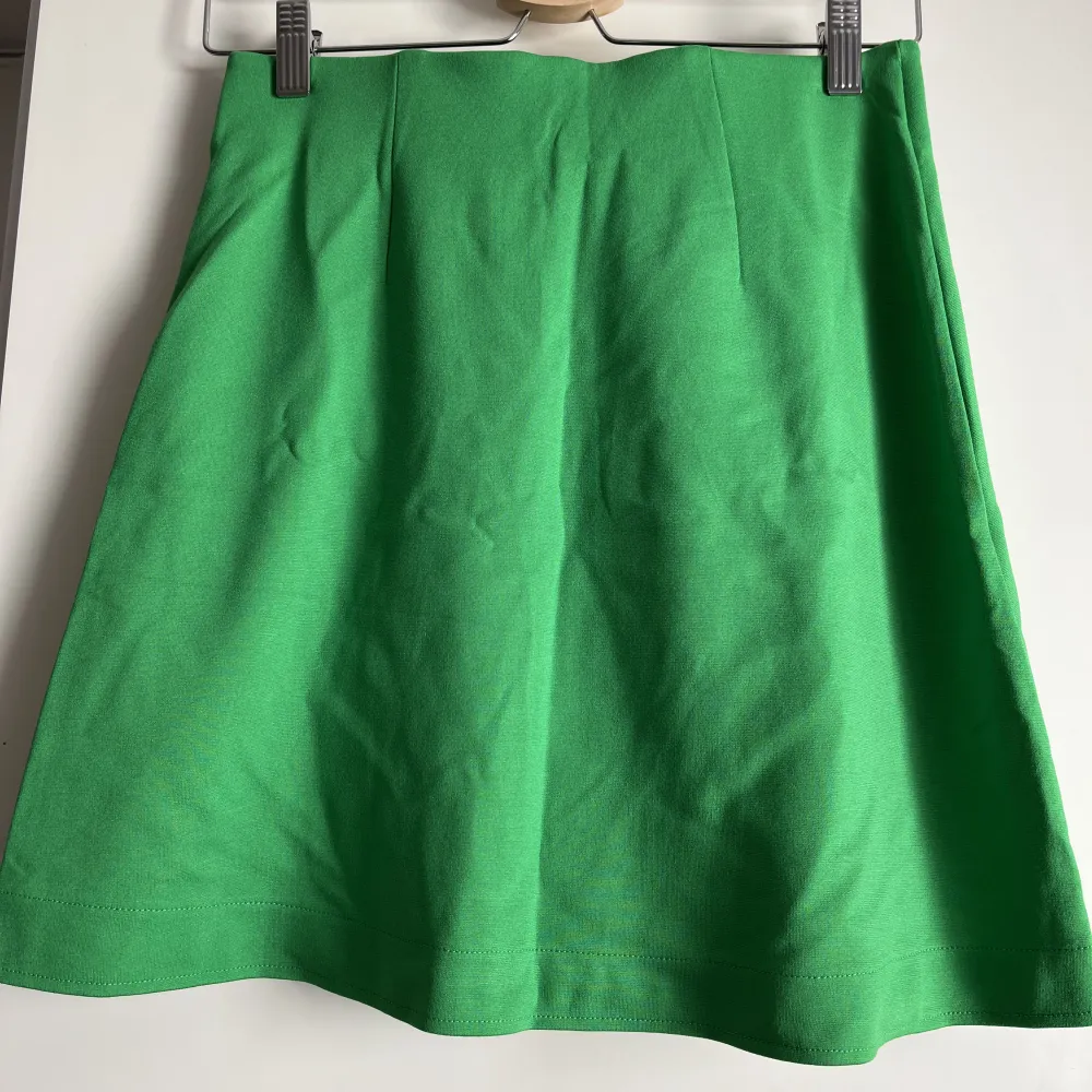 Klargrön kort kjol i mjukt stretchigt material. Tajt passform med liten slits. Ser ut som omlott, men är inte det egentligen. Aldrig använd, prislappen dock borttagen. . Kjolar.