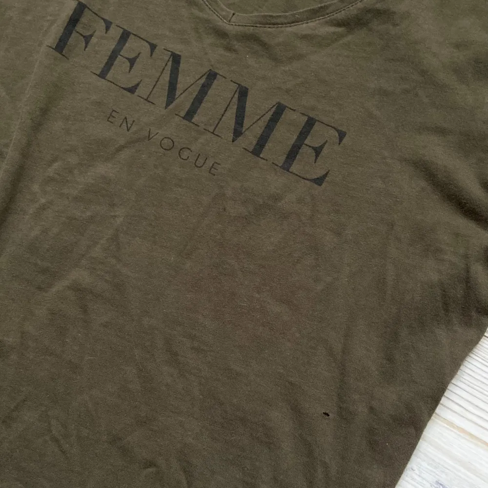 Superfin khakigrön t-shirt med v-ringning och texten ”Femme en Vogue” 🖤 Den har ett litet hål (se bild 2). Taggarna är bortklippta så vet inte storlek men skulle säga S/M!. T-shirts.