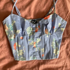 Korsett med blommigt mönster - Blått korsett med blommor från Zara i storleken Xs. Klädesplagget är i nyskick och inga defekter eller lukter förekommer. Fråga om flera bilder <3