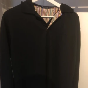 Svart skjorta från Paul Smith - En elegant svart skjorta från Paul Smith med en färgglad randig insida vid kragen. Skjortan har långa ärmar och en klassisk krage.