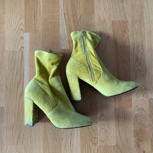 Gula klackar - Säljer mina häftiga klackar/boots som inte kommer till användning. Dragkedja intill och i stark gul färg. 10cm klackhöjd. En OBS på att ena klacken har repa i tyget, se sista bild! Därav väldigt billigt pris 🌻