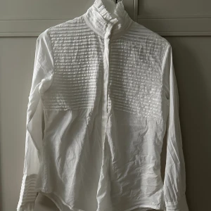 Vit blus  - Vit blus/skjorta men fin knäppning i ärmarna. Knappar hela vägen, går att styla på olika sätt. Lite mindre i storleken. Skulle säga att den passar XS-S (jag är en S). 