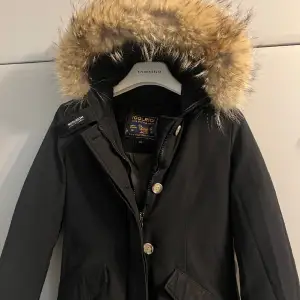 Jackan är en Woolrich arctic parka i storlek XS. Svart och äkta päls.  Jackan har enbart slitage på den sista bilden. Ett slitage på kroken som ska använda för att hänga upp sin jacka. Detta går att sy ganska enkelt. Annars i ett underbar skick 