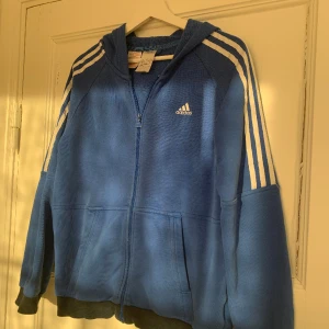 Adidas-Zipup  - Blå Zipup från Adidas med tryck på luvan. Den är för 13-14 år gamla barn, men sitter ungefär som S. Den har 3 små hål på ryggen som knappt syns (se sista bilden). 