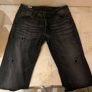 Jack and Jones jeans - Väldigt bra skick 9/10. Snygg färg som passar med allt. Feta slitningar på jeansen. Storlek 34/32. Ny pris 1199. Hör av dig vid frågor om passform osv. Obs vissa av slitningarna går igenom byxorna!! Priset är rörligt vid snabb affär!!