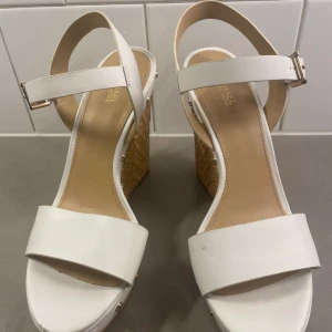 MICHAEL KORS Wedge vit/guld - Använda 1gång. Som nya. 7 1/2 i storlek. Vit läder med guldspänne. Gulddetaljer runt skorna, skulle tro 8-9  cm klack 