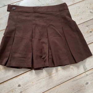 Kjol - Brun kjol från H&M med dragkedja på sidan och knapp. Bra skick, säljs då den inte används.