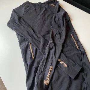 En funktions tröja🖤 - Säljer funktions tröja från Skins i stolek XS/34 i svart färg med guld ditaljer💛 Denna träningströjan är parfekt för utomhus löpning då den är tun i materialet och andas bra🖤 säljer denna då den inte passar längre och priset kan diskuteras💛