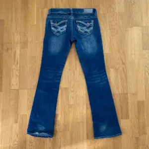 Jättesnygga lågmidjade bootcut jeans med coola fickor och detaljer! Lite skadade längst ner annars mycket bra skick. Midjemått 39cm innerbenslängd 82cm Skriv vid frågor💘🫶