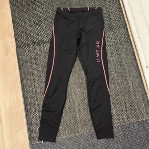 Träningstights med rosa detaljer  - Snygga tights med rosa ränder och text. Bakficka på rumpan och dragkedjor längst ned som man kan dra upp om man vill. Bra skick!