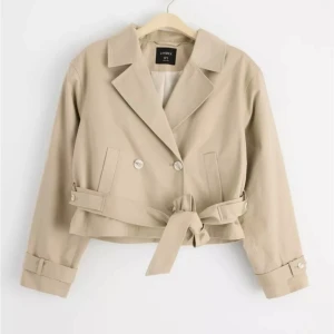 Trenchcoat - Croppad trenchcoat från Lindex, endast använd en gång, slutsåld på hemsidan. Nypris: 999kr. Mitt pris: 500kr.
