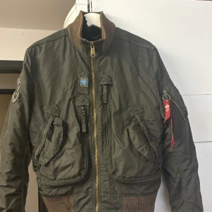 Alpha vår/höst jacka  - Fin gammal alpha som inte används många gr då den va alldeles förliten legat nerpackad några år men fint skick hel o ren, mörkgrön/skimrig  tror ny pris låg på 4700 då