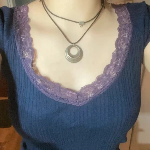 Tshirt med spets - Marinblå Tshirt med lila söegs detaljer kring urringningen. Köparen står för frakt. 