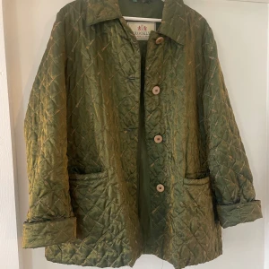 Grön jacka med glitterdetalj, quiltad - Quiltad jacka köpt second hand i Spanien. Märke Brooklyn. Fin kvalité, glansig olivgrön färg. Oversized på mig som är storlek S. 