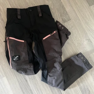 Revolution Race byxor - Säljer mina jättefina friluftsbyxor från Revolution Race i storlek XS, sparsamt använda i fint skick! Är svarta och mörkgråa med jättefina ljusrosa dragkedjor, den färgen säljs inte längre. Säljs då de blivit för små för mig tyvärr