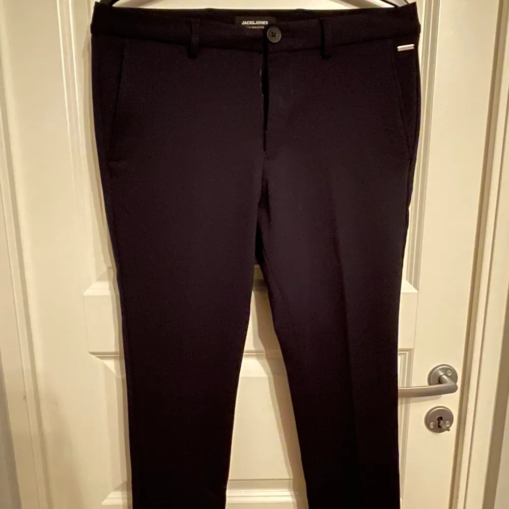 Svarta kostymbyxor från Jack & Jones. Två fickor framtill samt två fickor baktill, försluts med dragkedja och knapp.. Jeans & Byxor.