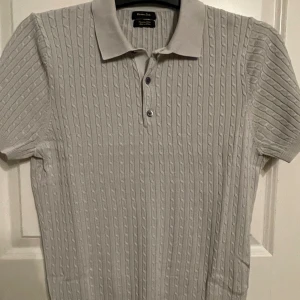 Kabelstickad piké-tröja - Grå piké-tröja från Massimo Dutti i kabelstickat mönster med tre knappar upptill. Använd fåtal gånger, väldigt fint skick.