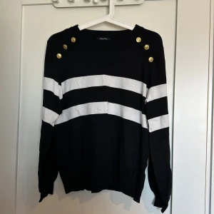 Långärmad tröja i fint skick  - Långärmad tunnt stickad tröja med detaljer på axlarna. Svart med vita och guldiga detaljer.  Djur finns i hemmet!