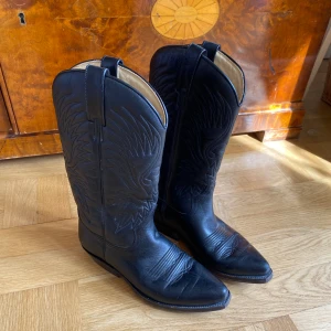 Svarta cowboystövlar - Skitcoola svarta cowboystövlar i läder! Köpt vintage. Stövlarna är ca 30 cm höga från marken, och slutar mitt på vaden.   Pris kan diskuteras. 