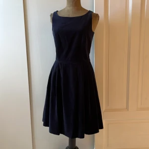 Mörkblå sammetsklänning från Hampton Republic - Säljer en superfin mörkblå sammetsklänning från Hampton Republic. Den är ärmlös och har en klassisk, elegant stil med dragkedja bak. Klänningen är gjord av 100% bomull med ett foder av 100% polyester, vilket gör den både bekväm och lätt att bära. Perfekt för höstens fester!