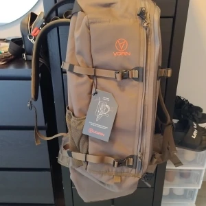 Brun ryggsäck från Vorn - En brun ryggsäck från Vorn, modell EV30. Ryggsäcken är designad för att bära och skydda vapen under jakt. Den har flera fack och justerbara remmar för bekväm passform.