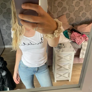 Vit t-shirt med text - Säljer en vit t-shirt med svart text på bröstet. T-shirten är ärmlös och har en rund halsringning. Perfekt för en avslappnad och stilren look. Passar bra till jeans eller kjol.