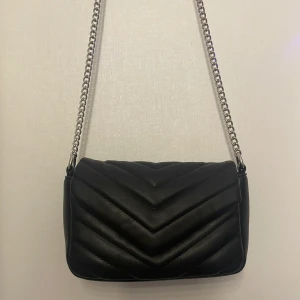  Väska - Säljer en snygg svart axelväska köpt på glitter för 250kr. Väskan har en silverfärgad kedja som axelrem som är lite missfärgad på ett ställe, kontakta mig för frågor och om intresserad 🩷