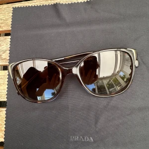 Prada solglasögon  - Prada solglasögon i mörk brunt. Självklart äkta. Kommer i Pradas påse, ej kartong. Saknar en liten guld detalj på ena bågen, inget överdrivet märkbart. Säljer därför för ett bra pris. Nypris på misterspex ca 3000kr