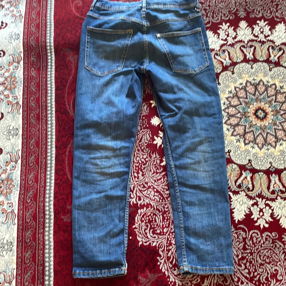 Säljer ett par blå jeansbyxor i relaxed fit. De är tillverkade av denim och har en tapered leg design. Byxorna är i storlek 152 och är tillverkade i Pakistan. Perfekta för en avslappnad och bekväm stil!. Jeans & Byxor.