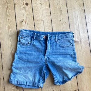 Blå jeansshorts - Säljer ett par snygga blå jeansshorts i storlek 32. De är i nyskick och perfekta för sommaren. Shortsen har en normal passform och är tillverkade av denim. De har klassisk femficksdesign och stängs med en knapp och dragkedja. Perfekta för en avslappnad och cool look! 🌞👖