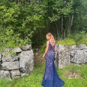 Mörkblå spetsklänning - Säljer en superfin mörkblå långklänning i spets (beige underklänning). Klänningen har en v-ringad rygg, boatneck framtill och är ärmlös, perfekt för bal, bröllop eller andra speciella tillfällen. Använd endast en gång, nyskick. Nypris 1500:-