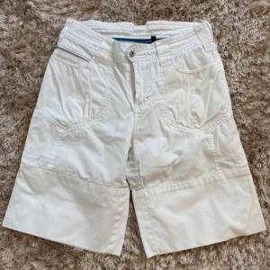 Vita shorts med fickor - Säljer ett par vita shorts med flera fickor fram och bak. De har en knapp och dragkedja framtill och är i bra skick Perfekta för sommaren!