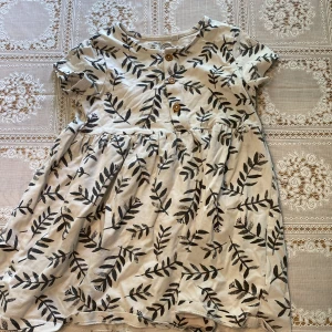 Vit klänning med blad - Vit klänning med blad-motiv från Lindex i storlek 86. Bild 1: framsidan  Bild 2: baksidan 