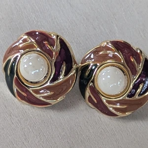 Färgglada örhängen med pärlor - Ett par runda clipsörhängen med en central pärla omgiven av ett virvlande mönster i guld, lila, svart och brunt. Örhängena har en elegant och unik design, Mycket Fint skick 