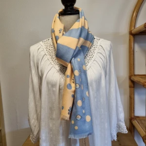 Blå och beige halsduk med prickigt mönster - En elegant halsduk i blått och beige med ett prickigt mönster. Halsduken har små detaljer av olika figurer och fransar i ändarna.